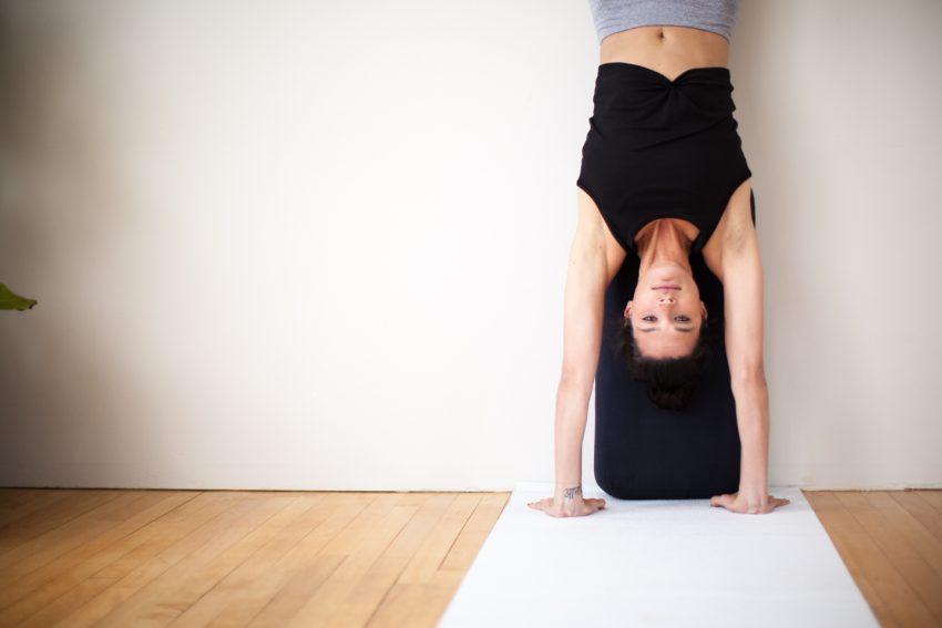 woman practices handstand inversion against a walll