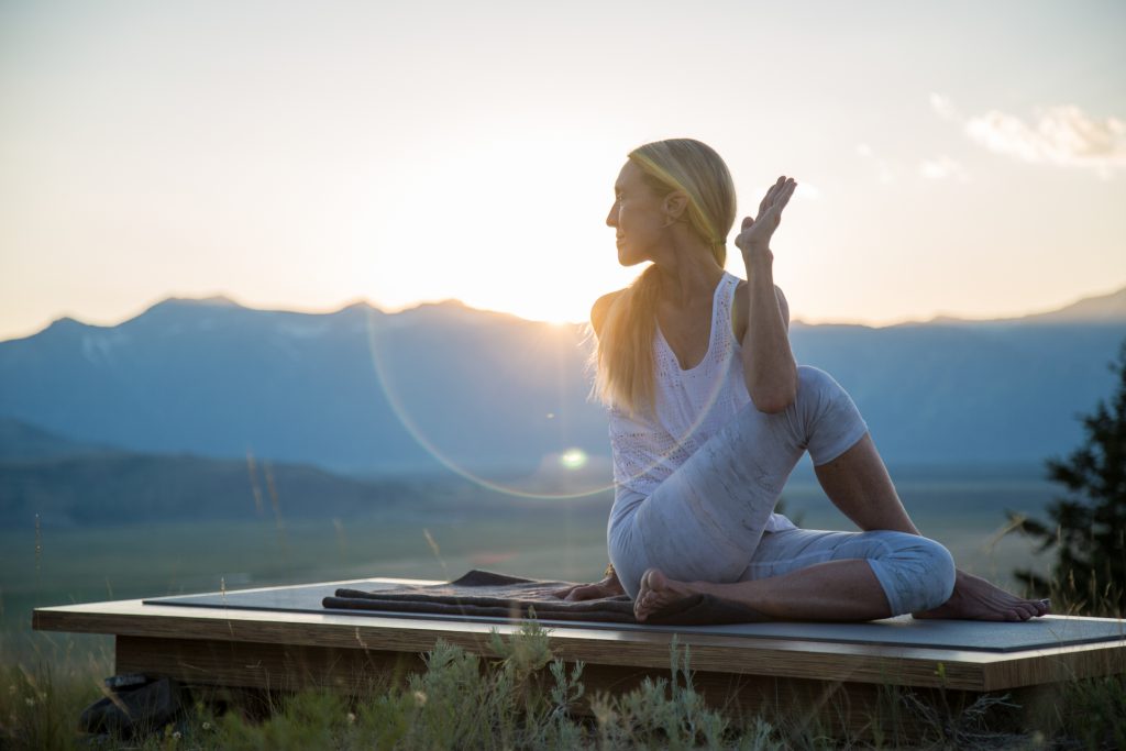 woman practicing yoga in all white clothing does a seated twist