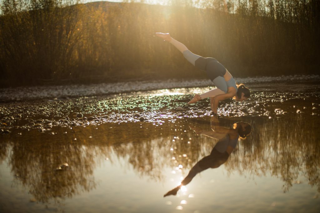 woman practices yoga near a reflective pond -yogatoday