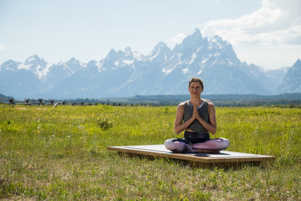 woman seated on a yoga mat outdoors with her hands in prayer position - yogatoday.com