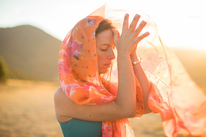woman with orange scarf presses her thumbs to the center of her forehead - yogatoday