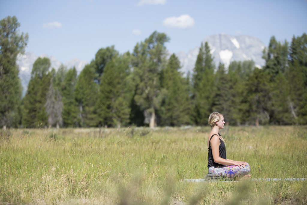 woman meditates while seated on an outdoor yoga platform in Grand Teton National Park -YogaToday