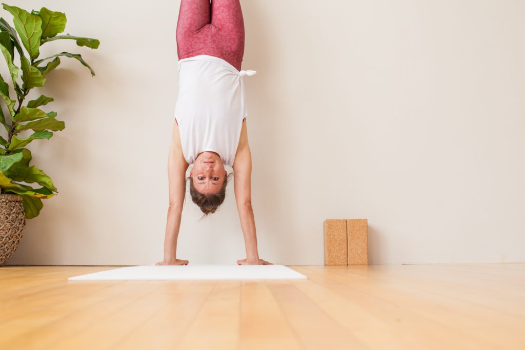 yoga teacher practices a handstand against a wall -yogatoday