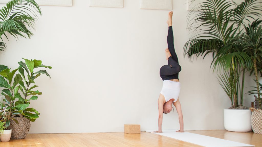 woman practices one legged handstand inversion against a wall -yogatoday